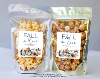 May include: Two clear plastic bags filled with popcorn. Each bag has a square label with the text "FALL in love" and a watercolor illustration of pumpkins and fall foliage. The text below the illustration reads "MADISON & MICHAEL 10.07.2023". The text at the bottom of the image reads "**POPCORN IS NOT INCLUDED** LISTING IS ONLY FOR BAGS & STICKERS"