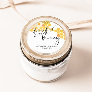 May include: A white jar with a gold lid and a round label that says "found my honey" with a bee and honeycomb design. The label also includes the names "Michael & Emma" and the date "09.03.23".