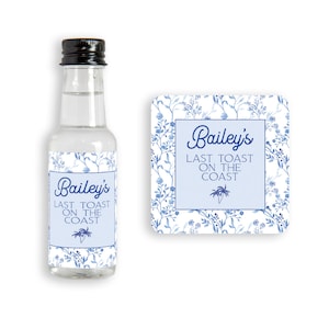 May include: A small clear glass bottle with a black lid and a blue and white floral label that says "Bailey's Last Toast on the Coast".  The bottle is next to a blue and white floral coaster with the same text.