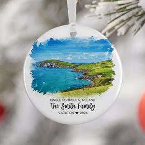 May include: A white ceramic ornament with a watercolor image of a coastal landscape. The text "Dingle Peninsula, Ireland The Smith Family Vacation 2024" is printed on the ornament.