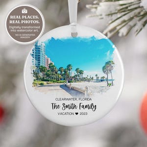 Könnte beinhalten: Ein runder, weißer Keramik-Weihnachtsbaumschmuck mit einer aquarellartigen Strandszene von Clearwater, Florida, inklusive Palmen und Gebäuden. Der Text lautet: CLEARWATER, FLORIDA, The Smith Family, VACATION 2023 mit einem Herz.