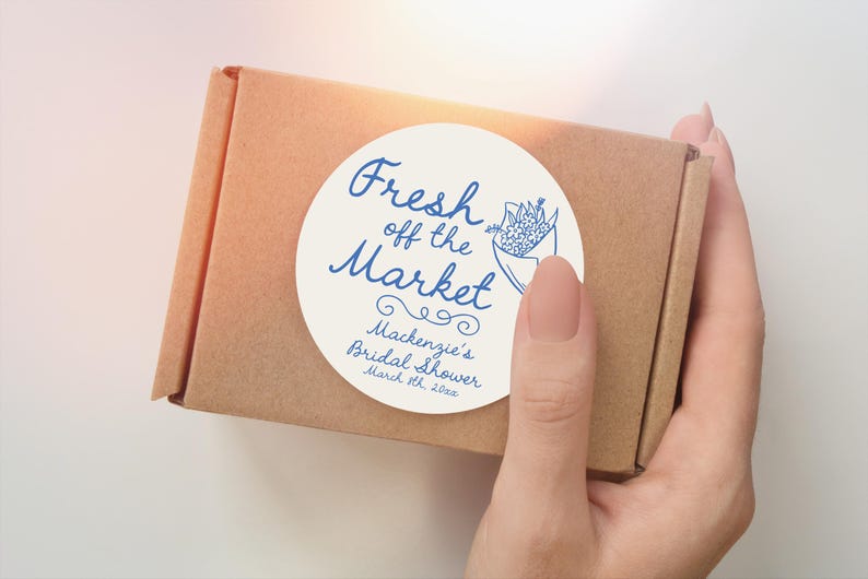 May include: White round sticker with blue text that reads "Fresh off the Market" with a stylized floral design. The sticker also includes the text "Mackenzie's Bridal Shower March 11th, 2023".