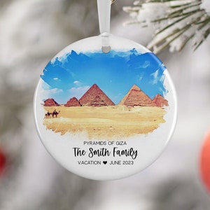 Könnte beinhalten: Ein runder weißer Keramik-Anhänger mit einem Aquarellbild der Pyramiden von Gizeh in Ägypten. Der Text "PYRAMIDS OF GIZA The Smith Family VACATION ♥ JUNE 2023" ist auf dem Anhänger gedruckt.