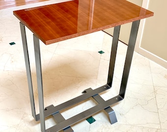 May include: A modern side table with a rectangular, glossy, reddish-brown wooden top. The table has a minimalist design with gray metal legs and a supporting structure. The legs are U-shaped, and the base has a grid-like design.