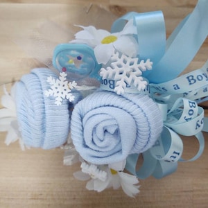 May include: A baby shower centerpiece made of blue rolled socks, white flowers, and blue ribbon with the text "It's a Boy" printed on it.