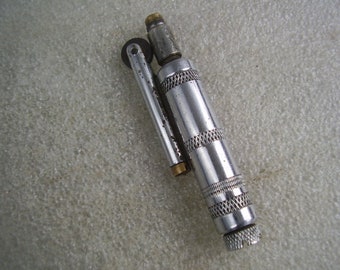 Peut inclure: Un briquet en métal argenté avec une roue sur le côté et un petit bouton rond en argent à l'extrémité.