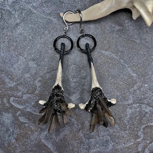May include: A pair of black and white bone earrings with a cluster of smoky quartz crystals at the bottom.