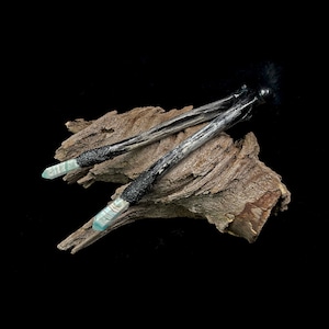 May include: Two black and silver wands with blue and white crystal tips, resting on a piece of weathered driftwood.