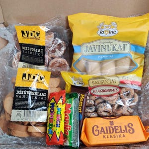 Puede incluir: Surtido de aperitivos envasados que incluyen galletas de jengibre, obleas de vainilla, anillos de pretzel y barras de chocolate. Los envases llevan los nombres de marca "JDC", "Jainė", "Hemat", "Maniia", "Nomeda" y "Gaidelis".