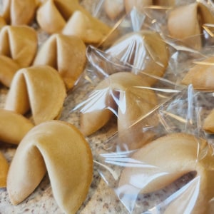 Puede incluir: Una colecci&oacute;n de galletas de la fortuna en forma de media luna de color marr&oacute;n dorado. Varias de las galletas est&aacute;n envueltas individualmente en pl&aacute;stico transparente arrugado, mientras que otras est&aacute;n sin envolver.
