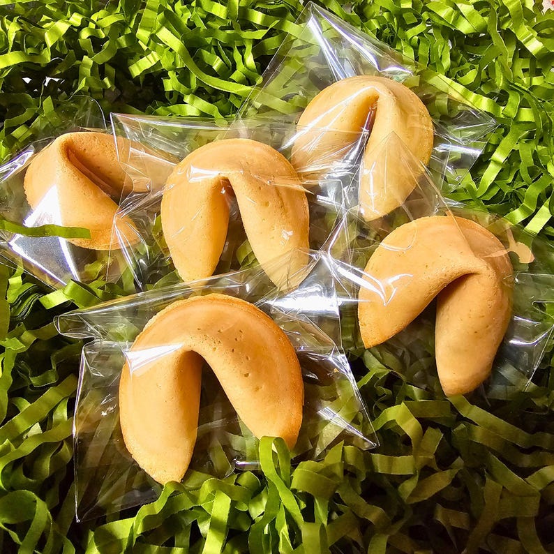 Puede incluir: Cinco galletas de la fortuna de color marr&oacute;n dorado, cada una envuelta individualmente en una bolsa de pl&aacute;stico transparente. Las galletas tienen una forma curva y plegada con una textura horneada suave. Est&aacute;n dispuestas en grupo, mostrando su color tostado.