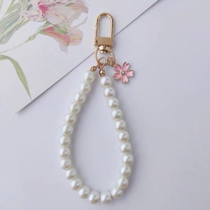 May include: A gold keychain with a pearl chain and a pink flower charm.