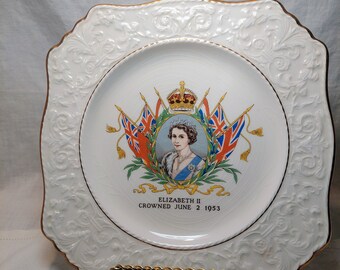 Puede incluir: Plato conmemorativo de cerámica blanca con borde dorado y diseño floral en relieve. En el centro, un retrato de la reina Isabel II con el texto "Elizabeth II Crowned June 2 1953".