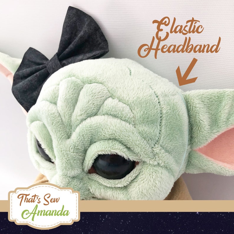 May include: A green plush toy with large eyes and a black bow headband. The headband is elastic and says "Elastic Headband" in brown text.