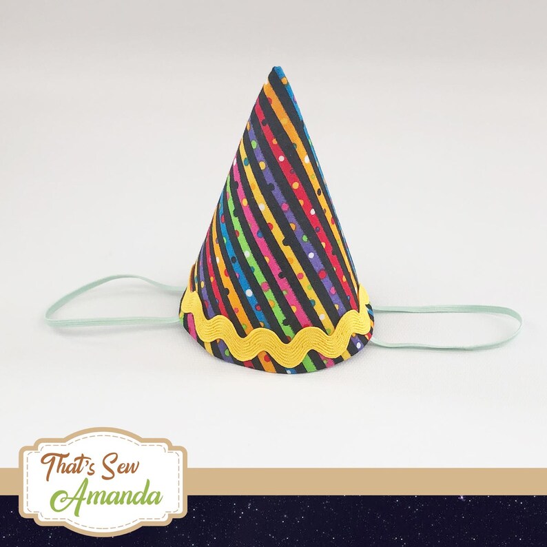May include: A colorful party hat with black stripes, rainbow stripes, and polka dots. The hat has a yellow scalloped trim and a light green elastic band.