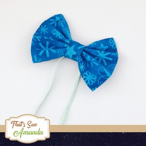 May include: A blue bow tie with a snowflake pattern. The bow tie is tied with a light blue ribbon.