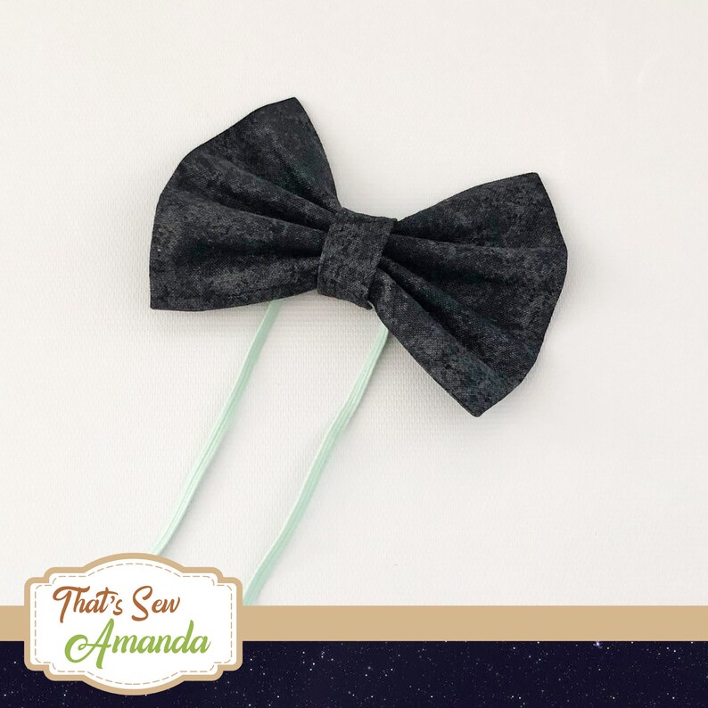 May include: A black bow tie with a textured fabric and light green elastic straps.