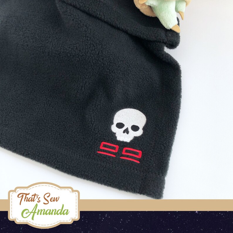 May include: Black fleece fabric with a white skull and crossbones embroidered design. The crossbones are red.