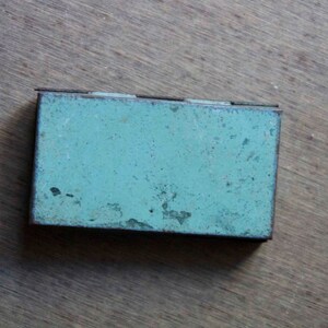 Peut inclure: Une petite bo&icirc;te rectangulaire en m&eacute;tal de couleur bleu-vert avec une finition us&eacute;e et vieillie. La bo&icirc;te a un couvercle &agrave; charni&egrave;re et semble &ecirc;tre vintage.