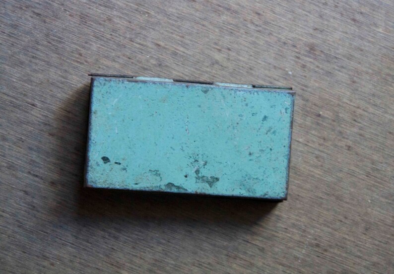 Peut inclure: Une petite bo&icirc;te rectangulaire en m&eacute;tal de couleur bleu-vert avec une finition us&eacute;e et vieillie. La bo&icirc;te a un couvercle &agrave; charni&egrave;re et semble &ecirc;tre vintage.
