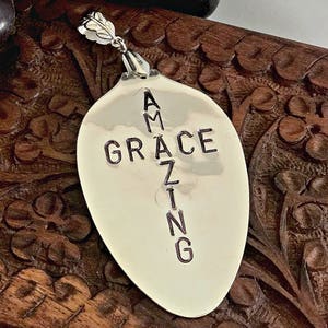 May include: Silver spoon pendant with the words "Amazing Grace" engraved on it. The spoon is shaped like a cross.