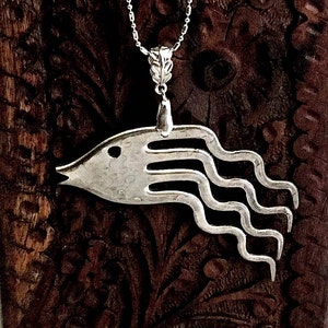 May include: Silver necklace with a pendant shaped like a fish with wavy lines coming out of its head. The pendant is made from a repurposed fork.