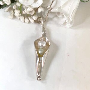 May include: A silver necklace with a pea pod pendant. The pendant is made from a spoon and holds three white pearls inside.