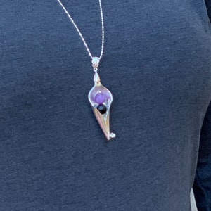 May include: A silver necklace with a pendant shaped like a flower. The flower is open and has a purple and black stone inside.
