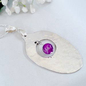 Puede incluir: Un collar con un colgante de cuchara de plata martillada con una piedra de &aacute;gata p&uacute;rpura que cuelga de un c&iacute;rculo cortado en la cuchara.