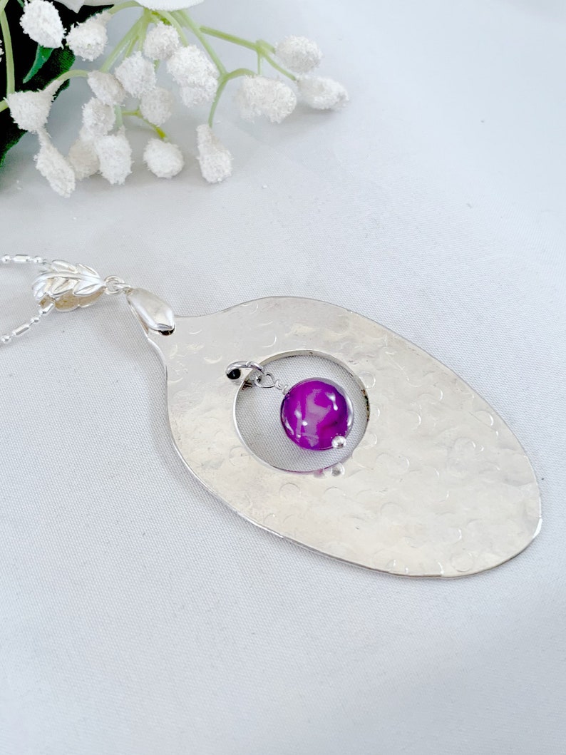 Puede incluir: Un collar con un colgante de cuchara de plata martillada con una piedra de &aacute;gata p&uacute;rpura que cuelga de un c&iacute;rculo cortado en la cuchara.