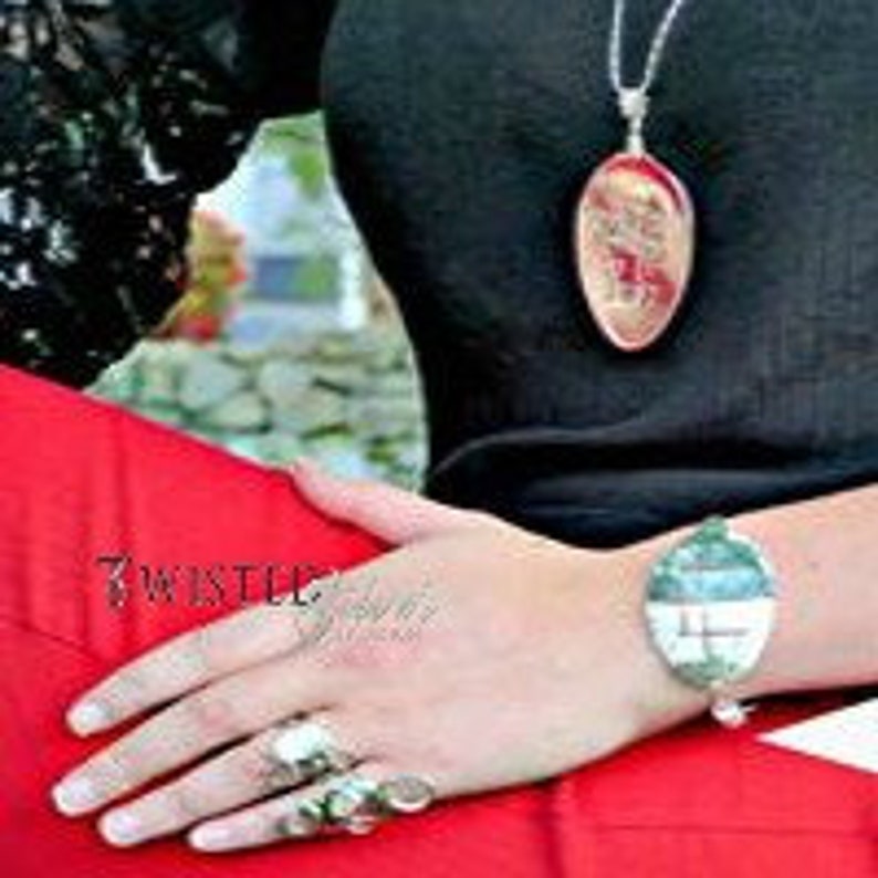 Puede incluir: Un collar de cuchara de plata con un dise&ntilde;o floral. La cuchara es de forma ovalada y cuelga de una cadena de plata. El collar lo lleva una persona con una camisa negra y pantalones rojos.