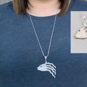 May include: A silver necklace with a pendant shaped like a fish with flowing fins. The pendant is made of metal and has a textured surface.