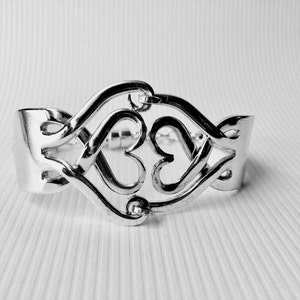 May include: Silver bracelet with a double heart design. The hearts are intertwined and create a delicate and intricate pattern.