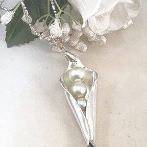 May include: A silver necklace with a pea pod pendant containing three white pearls.