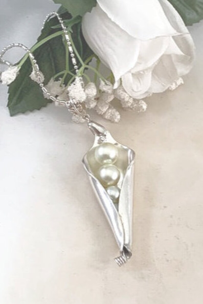 May include: A silver necklace with a pea pod pendant containing three white pearls.
