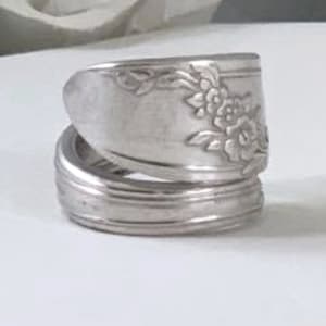 May include: A silver ring made from a repurposed spoon with a floral design. The ring is made of two pieces of spoon that are wrapped around each other.