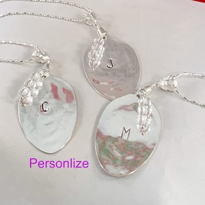 May include: Three silver spoon necklaces with initial charms. The spoons are oval shaped and have a hammered texture. The charms are attached to the spoons with a chain and have a beaded design. The initials on the spoons are J, C, and M.