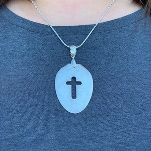 Puede incluir: Un collar de cadena de plata con un colgante con forma de cuchara con una cruz recortada en el centro.