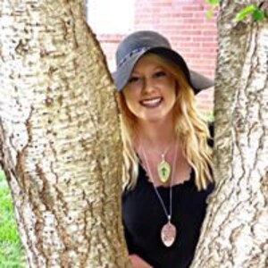 Puede incluir: Una mujer con un sombrero negro y una blusa negra con dos collares de plata. Los collares tienen un colgante en forma de hoja con un dise&ntilde;o de cruz.