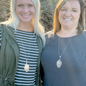 May include: Two women wearing striped and gray shirts with silver spoon necklaces. The spoons are shaped like an oval and have a textured surface.