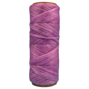 May include: A spool of purple and lavender colored yarn. The yarn is wound tightly around the spool and has a slightly textured surface.