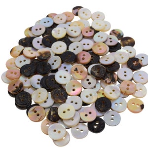 May include: A pile of round, two-hole buttons made from natural shell. The buttons are in various shades of brown, white, and pink.