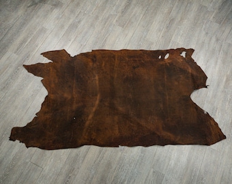 May include: A large, brown leather hide with a natural, irregular shape. The hide has a rustic, distressed look and is suitable for crafting or decorating.
