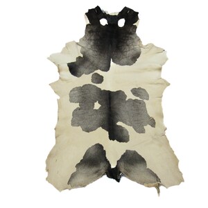 May include: A cowhide rug with a unique pattern. The rug features a cream-colored background with large, irregular black blotches. The hide has a natural, uneven edge, adding to its rustic charm. This decorative rug is suitable for home decor.