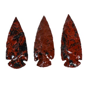 May include: Three arrowheads made of red jasper with black veins. The arrowheads are pointed and have a smooth, polished finish.