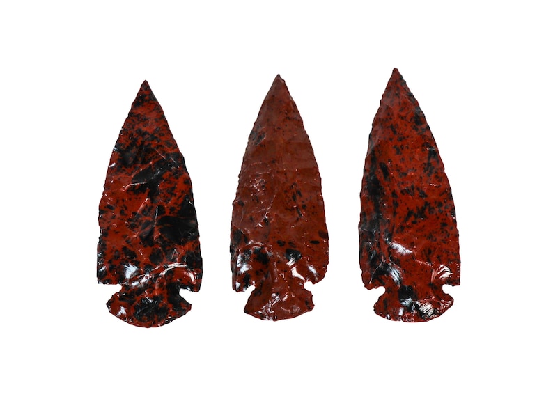 May include: Three arrowheads made of red jasper with black veins. The arrowheads are pointed and have a smooth, polished finish.