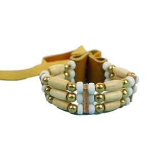 May include: A brown leather bracelet with three rows of beads. The beads are white, gold, and wooden.