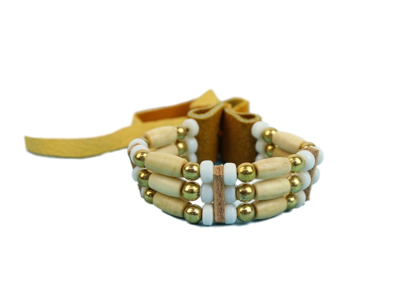 May include: A brown leather bracelet with three rows of beads. The beads are white, gold, and wooden.