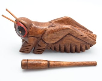 May include: A wooden carved grasshopper with red eyes and a wooden stick. The grasshopper is a musical instrument.