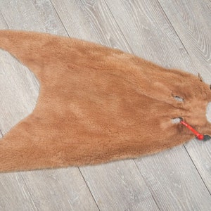 May include: A brown fur pelt with a small hole in the center. The fur is soft and fluffy.